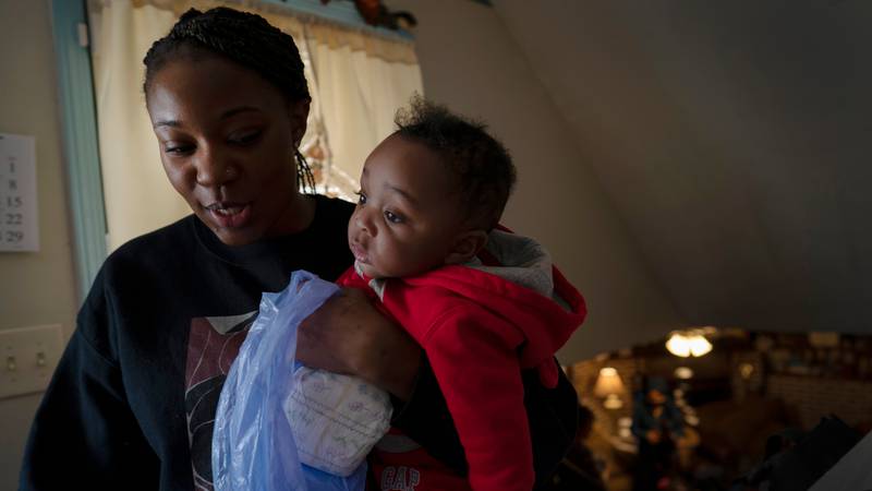Ansonia Lyons carries her son, Adrien Lyons, as she takes him for a diaper change in...